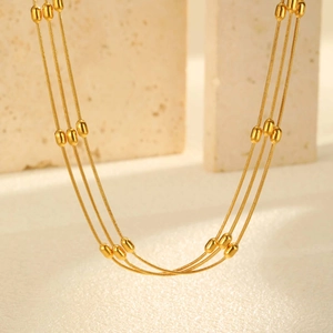 Detailed macro shot of triple-layer gold beaded snake chain necklace over beige stone
