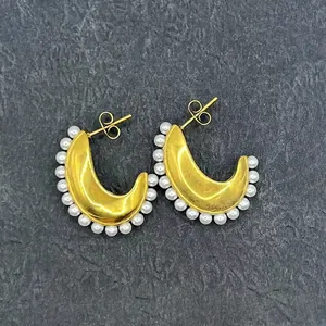 Macro detail of crescent gold earrings with pearl edges on dark textured stone