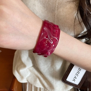 Detailed close-up of wide acrylic bangle with dark pink marble texture and pleated design