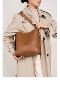 Detail einer braunen Leder-Eimertasche mit verstellbarem Gurt über einem beigen Mantel