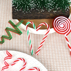 Christmas red, green and white candy cane and lollipop ornaments hanging on a snowy pine branch