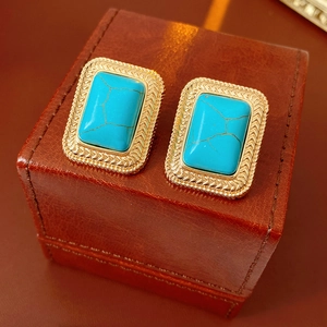 Macro di orecchini vintage con turchese blu e bordi intrecciati dorati su scatola marrone