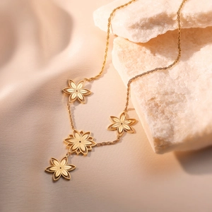 Minimalist gold-plated flower pendant necklace on white stones with warm lighting