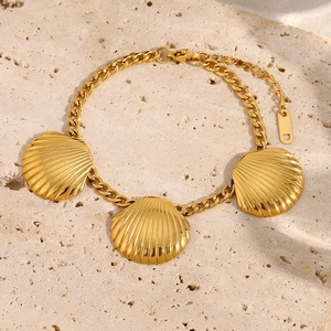 Detailed view of three gold scallop shells on a stainless steel bracelet over stone