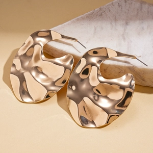 Détail macro de boucles d'oreilles dorées irrégulières avec texture miroir martelée