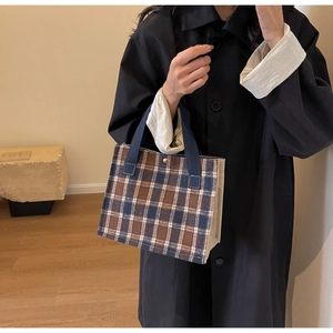 Brown and blue plaid canvas tote bag held by a model wearing a stylish black trench coat
