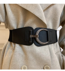 Detail of vintage wide black leather belt with ornate round metal buckle on a beige coat