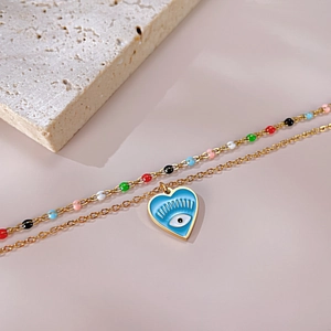 Golden heart necklace with evil eye pendant and colorful beads on a beige stone base