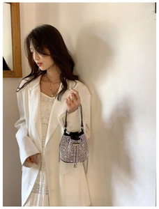 Close-up of sparkling silver rhinestone bucket bag with black leather handle on white blazer