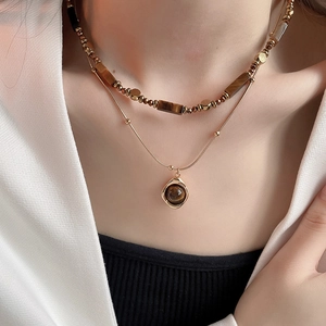 Close-up of double-layered gold-plated necklace with tiger eye stone and circular pendant