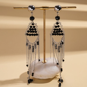 Detail view of geometric chain tassel earrings with black beads on a jewelry stand