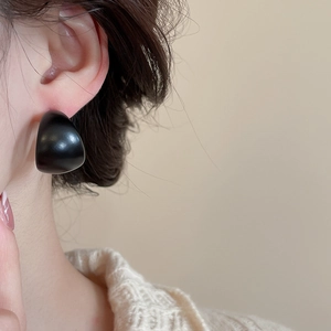 Close-up of a minimalist black acrylic C-shaped earring worn on a model ear