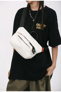 Detail of white canvas crossbody bag with orange logo tag and wide nylon strap