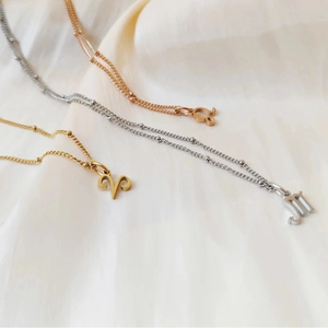 Close-up of gold, rose gold and silver zodiac necklaces on white silk fabric background
