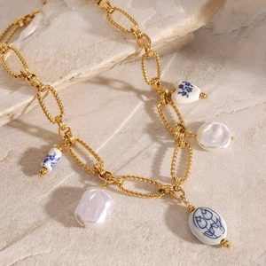 Gold chain necklace with irregular white pearls and blue ceramic heart pendants on stone
