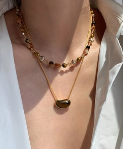 Detail of layered gold necklaces with brown tiger eye stone pendant and colorful beads
