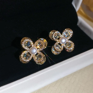 Vue détaillée de boucles d'oreilles fleurs dorées avec perle centrale et zircons brillants