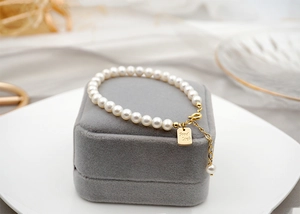 Detail of freshwater pearl bracelet with gold Good Luck tag on grey velvet display