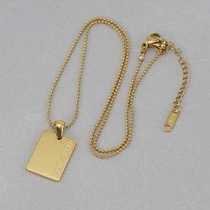Macro shot of gold square pendant engraved with BREATHE on a stylish bead chain necklace