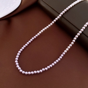 Macro shot of high-luster lavender pearl necklace on dark leather and white ceramic tray