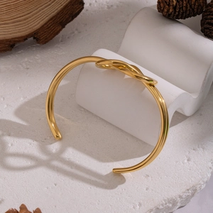 Minimalist 18K gold plated knotted open bangle bracelet on a white stone background