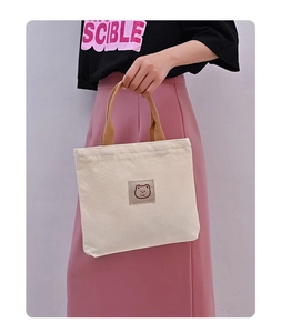 Close-up of canvas tote bag featuring embroidered bear detail and brown nylon handles