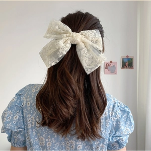 Elegant beige lace bow hair clip with floral embroidery on a female model