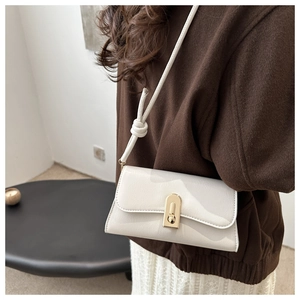 Close-up of white leather handbag featuring a gold metal lock and knotted strap detail