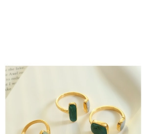 Detailed view of three gold titanium rings with rectangular green gemstones on a book