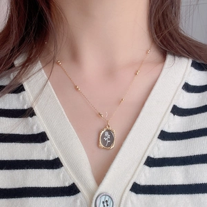 Detail view of a golden rectangle pendant with rose relief and bead chain on clothing