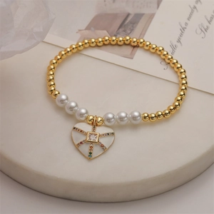 Dettaglio di bracciale con perle bianche e ciondolo a cuore in smalto su marmo