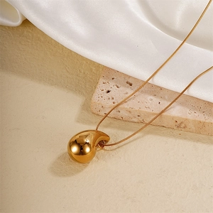 Detailed view of golden teardrop pendant on snake chain over white silk and stone textures
