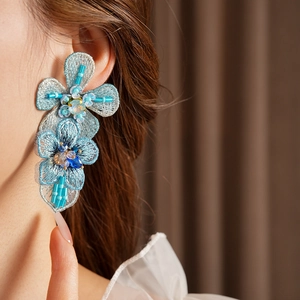 Close-up of blue embroidered floral earrings with crystals and beads worn by a model