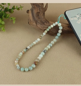 Detail of beaded phone lanyard with blue and neutral tones on a natural wood branch