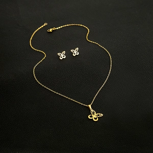 Close-up of golden hollow butterfly necklace and earrings set on textured black background