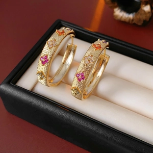 Détail de créoles plaquées or 18 carats avec fleurs en zircon coloré en écrin