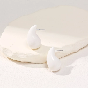Detail view of white teardrop stud earrings on a textured stone aesthetic background
