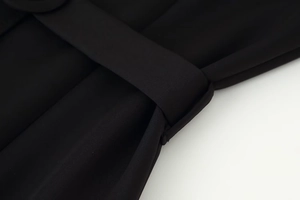 Detailed close-up of matte black fabric texture and belt stitching on a dress