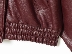 Detailed macro view of burgundy faux leather texture and elastic hem stitching on the jacket