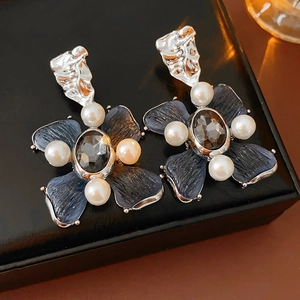 Macro shot of vintage flower earrings with blue petals and pearls on black leather box