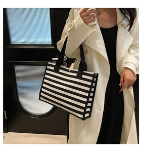 Dettaglio della tracolla nera di una borsa tote in tela a righe indossata da una modella