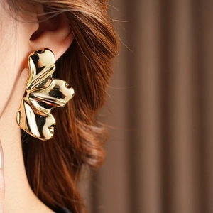 Close-up of golden irregular leaf earrings with textured metallic finish on model