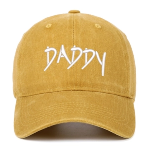 Close-up of white DADDY embroidery on a washed mustard yellow cotton baseball cap