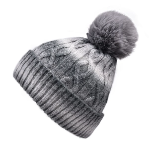 Macro detail of thick cable knit pattern and soft faux fur pom-pom on gradient winter hat