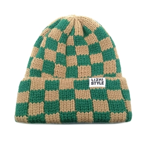 Detail of green and khaki checkerboard knit beanie with a white square logo patch