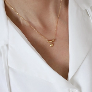 Elegant 18K gold-plated titanium necklace featuring a bow and heart pendant on model