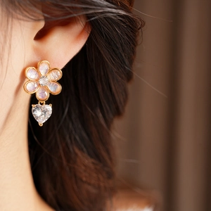Close-up of model wearing flower resin earrings with heart zirconia drops in gold