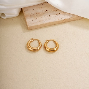 Polished gold titanium steel hoop earrings on light textured surface with silk decor