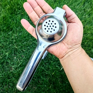 Handheld stainless steel lemon squeezer being held over a natural grass background
