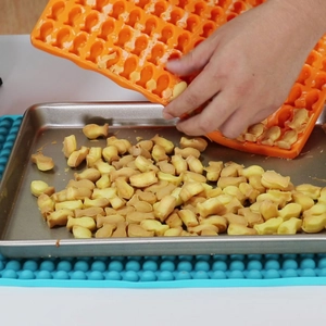 Flexible orange silicone mold releasing fish-shaped golden dog treats onto a baking tray